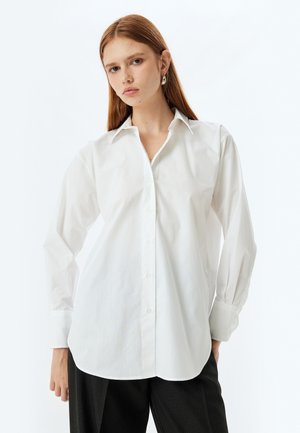 Camicia bianca con colletto, maniche lunghe, tessuto morbido, vestibilità su misura e leggero arricciatura sulle spalle.