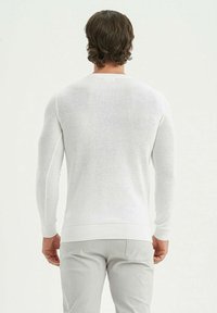 Pull en tricot blanc à manches longues, col rond, avec des poignets et un ourlet côtelés. Texture légère, design ajusté, sans motifs ni accents.