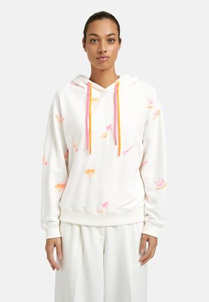 Woman wearing a white hoodie with pink and orange palm tree patterns and dual-colored pink and orange drawstrings, paired with white pants.
