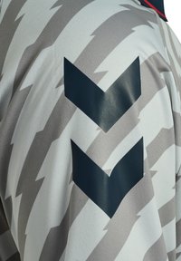 Tissu blanc et gris à motif en zigzag avec deux grandes flèches chevrons bleu foncé pointant vers le bas sur la manche, faisant partie d'un vêtement.