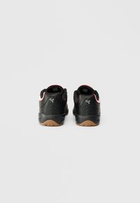 Un cuplu de sneakers negri Puma cu accente roșii și albe, văzuți din spate pe un fundal simplu de gri deschis.