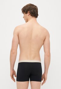 Črne hlačke z bež elastičnim pasom, izdelane iz gladkega materiala, se tesno prilegajo in prikazujejo preprost in običajen dizajn.