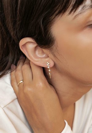Gold earrings with a linear design featuring small, sparkling gemstones arranged in a cascading pattern. Smooth finish.