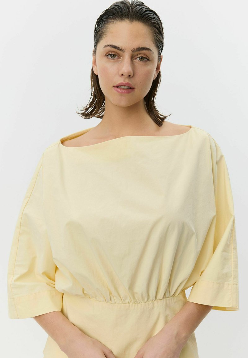 Gul bomuldstop med skulderfri halsudskæring og elastik i taljen, med korte, brede ærmer og en glat, let tekstur.