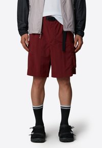 Maroon cargo shorts with pockets, a black belt, and a smooth texture. Black sandals and knee-high socks, featuring gray stripes.