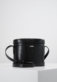 Pyöreä musta tekonahkainen käsilaukku, jossa on krokotiilinamainen texture, hopeiset yksityiskohdat ja säädettävä olkahihna. Varustettu turvallisella vetoketjulla ja sylinterimuotoisella rakenteella.