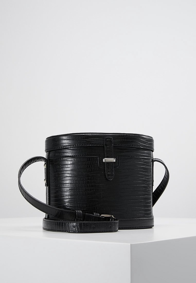 Pyöreä musta tekonahkainen käsilaukku, jossa on krokotiilinamainen texture, hopeiset yksityiskohdat ja säädettävä olkahihna. Varustettu turvallisella vetoketjulla ja sylinterimuotoisella rakenteella.