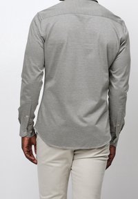 Grå långärmad skjorta med texturerad tyg, skräddarsydd passform och knappmanschetter. Har ett subtilt mönster och en rundad nederkant.