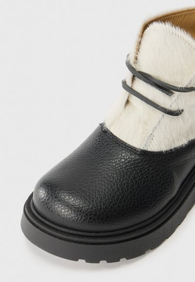 Svart läderankelboot med texturerad yta, med en vit päroverdel, svarta snören och en robust sula.