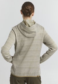 Sweat à capuche en tissu beige texturé avec des motifs géométriques blancs, avec un col zippé et des poignets, porté à l'envers.