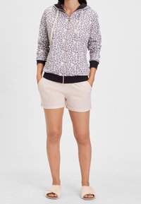Mikina na zip s leopardím potiskem v světle šedé a černé barvě, kombinována s béžovými šortkami. Obsahuje klokaní kapsu a má jemnou texturu.