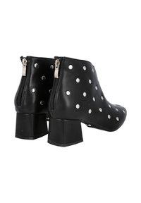 Botines de cuero negro con detalles de tachuelas plateadas, cremalleras laterales y tacón grueso de bloque. Textura suave con diseño de punta redondeada.