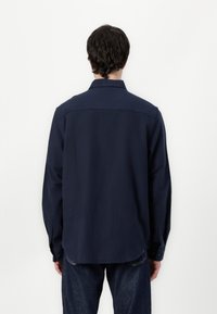 Navy long-sleeve shirt made of cotton, featuring a standard collar and button cuffs, with a straight back yoke and rounded hem.