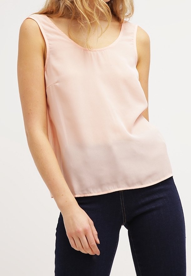 Vaaleanpunainen hihaton toppi sileästä kankaasta, jossa on pyöreä pääntie ja väljä malli, yhdistettynä tummiin farkkuihin.