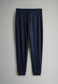Pantalones de chándal de canalé azul marino con cintura elástica y cordón, piernas entalladas y tobillos acampanados sobre un fondo gris.