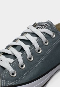 Μπλε πάνινο αθλητικό παπούτσι με λευκά κορδόνια, μεταλλικές τρύπες, λαστιχένια σόλα και αντιθετικές ραφές. Κοντινή άποψη του επάνω μέρους, που δείχνει την ετικέτα της μάρκας.