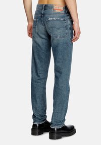 Blue denim jeans with a worn texture, straight fit, visible seams, two back pockets, and a branded leather patch at the waist.