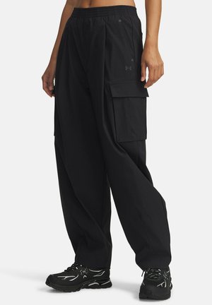 Persoon draagt losse zwarte cargobroek met elastische taille en zwarte sportieve sneakers met witte details.