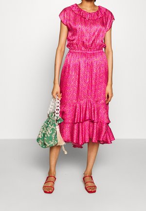 Vestido de estampado de leopardo rosa con escote volado y capas. Combinado con un bolso de patrón verde y sandalias planas rojas. Tejido texturizado.