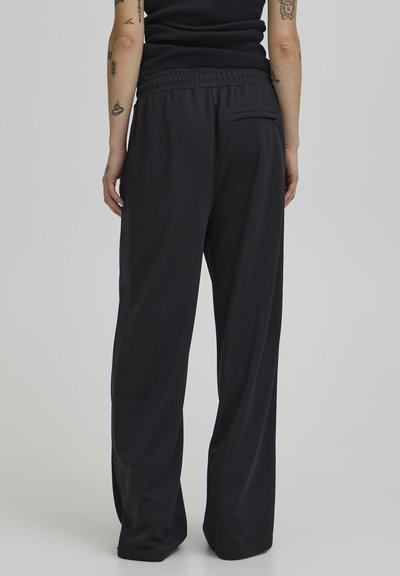 Pantalones de chándal negros, de corte holgado, con tela texturizada, cinturilla elástica, bolsillos laterales y un bolsillo trasero en el lado derecho.