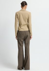 Camicia beige a maniche lunghe con tessuto testurizzato, abbinata a pantaloni marroni a quadri con design a gamba larga e sottili righe di profilo.