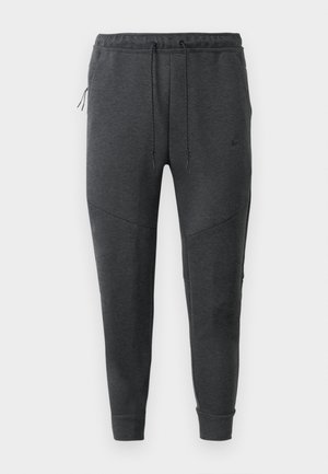 Pantalones jogger Nike de color gris oscuro con cordón en la cintura, bolsillo lateral con cremallera, piernas ajustadas y puños acanalados sobre un fondo blanco.