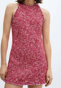 Robe halter en tricot dans un mélange texturé de rouge et blanc, présentant une coupe ajustée et un ourlet effiloché. Tissu lisse avec un léger éclat.