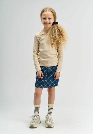 Bežs ribots garām piedurknēm tops ar ziedu rakstu, apvienots ar džinsa svārkiem, kas raksturo balti rombveida raksti, svītrainām ceļgala augstām zeķēm un sporta apaviem.