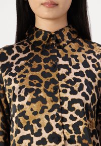 Leopardenmuster-Bluse mit einem schwarz-braunen Muster, ausgestattet mit einem Kragen und Knopfverschlüssen, aus glattem Stoff gefertigt.