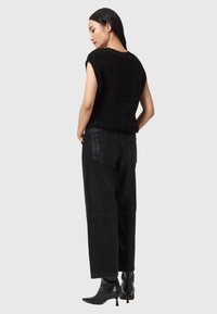 Top senza maniche in maglia nera abbinato a pantaloni neri a vita alta. I pantaloni hanno una finitura testurizzata e tasche posteriori. Stivali neri con tacco completano il look.