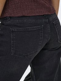 Personne portant un jean denim noir avec des poches arrière et un haut court texturé de couleur bordeaux foncé.