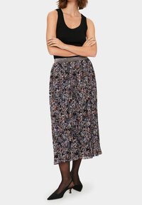 Svart linne parat med en flödande, mönstrad maxikjol med en flerfärgad blomsterdesign och ett metalliskt midjeband. Svarta klackskor.