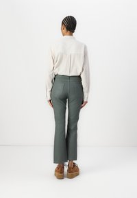 Lys beige langermet skjorte med en lett teksturert overflate, kombinert med høyt midjebånd, mørkegrønne flarebukser og lyse plattformsko.
