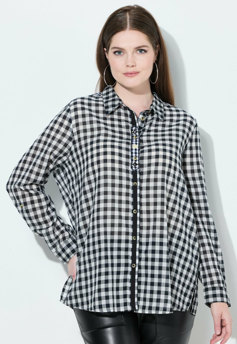 Zwart-wit geblokte blouse met een knoopsluiting aan de voorkant en lange mouwen. Voorzien van een kraag en decoratieve zwarte afwerking langs de knoopsluiting.