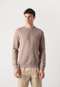 Sweatshirt marron à manches longues, col rond, avec un petit logo et un détail en V sur la poitrine. Tissu à texture lisse.
