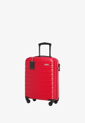 Valise rigide rouge avec un design nervuré, poignée noire rétractable, quatre roues et une étiquette attachée. Matériau durable, forme compacte.