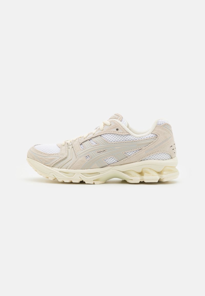 Baskets de sport beige et blanche en mesh avec semelle amortissante et design à lacets, présentées de côté sur un fond uni.
