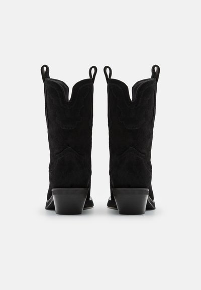 Botas de vaquero de ante negro con puntera afilada, bordes superiores curvados y lengüetas de tirón. Presentan detalles de costura y un tacón bajo en bloque.