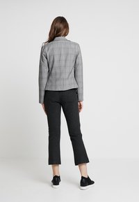 Blazer grigio a quadri con taglio su misura, abbinato a pantaloni neri a taglio cropped. L'ensemble è completato da sneakers nere slip-on.