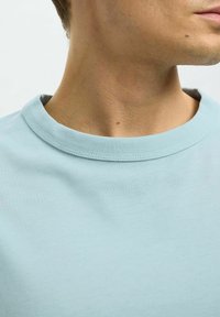 Ljusblå bomullströja med rund halsringning och korta ärmar, med en mjuk textur och synlig sömnad på kragen.