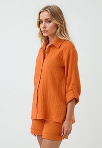Oranje gekreukt shirt met een kraag, knoopsluiting aan de voorkant en opgerolde mouwen, gecombineerd met bijpassende shorts, voorzien van een textuurstof.