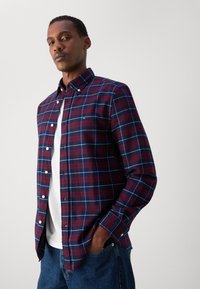 Camisa de cuadros roja y azul marino, con cuello, mangas largas y un corte regular, llevada sobre una camiseta blanca con jeans azules.