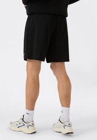 Pantaloni sportivi neri in rete con vita elasticizzata e logo Champion. Indossati con scarpe da ginnastica chiare e calze di lunghezza media.