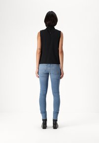 Svart ärmlös topp med hög hals och nyckelhål bak, kombinerad med blå tight jeans och svarta blockklackade ankelstövlar.