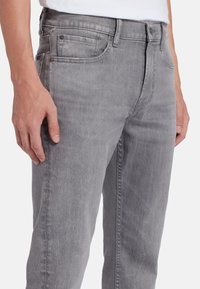 Jeans in denim grigio con un design aderente, cinque tasche e discreti dettagli di whiskering. Realizzati in materiale morbido e leggero.