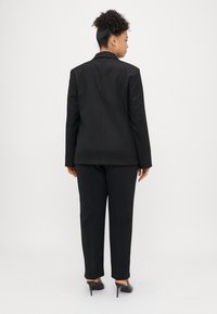 Μαύρο σακάκι και παντελόνι, με κομψή εφαρμογή. Λείος υφασμάτινος ιστό, κλασικός σχεδιασμός. Μικρές λάπιες και λεπτοί ώμοι. Κλειστές γόβες.