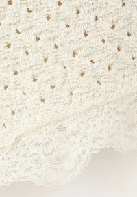 Tissu tricoté de couleur crème avec des trous en forme de losange et une bordure en dentelle festonnée le long du bord.