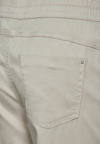 Primer plano de pantalones beige que muestran un bolsillo trasero con remache metálico y detalle de cintura elástica.