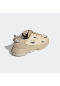 Světlé béžové tenisky Adidas s robustní podrážkou, síťovinovým větráním, tkaničkami a štítkem "Originals" na patě na bílém pozadí.