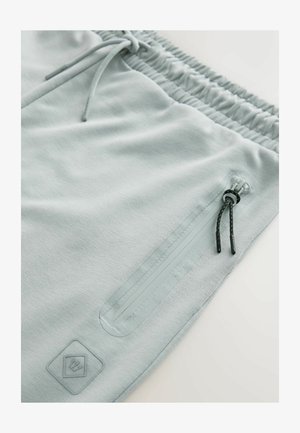 I pantaloni della tuta grigi chiari presentano un tessuto testurizzato, una vita elastica e una tasca con zip con accenti neri e lacci regolabili.